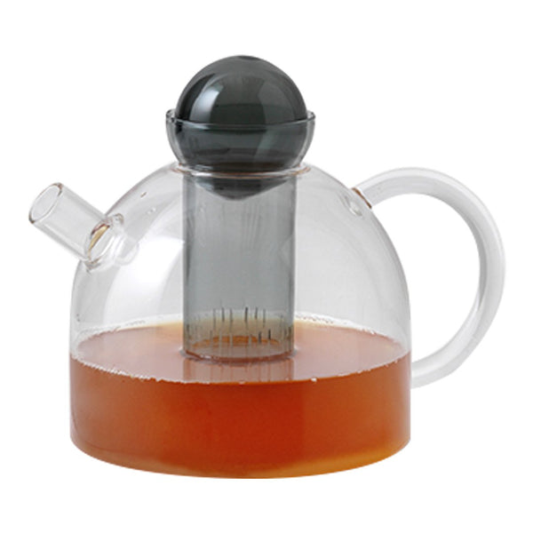 Clear glass teapot with a dome shape, black infuser, and rich amber tea, showcasing a modern and elegant design.