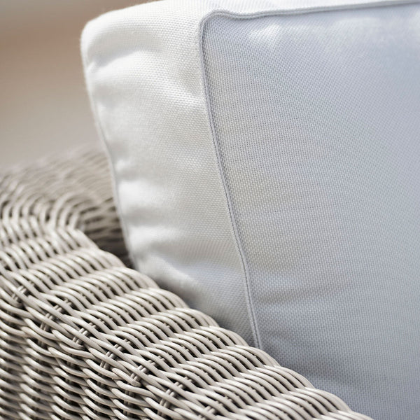 Neutral gray wicker chair with a smooth white pillow and subtle gray piping, creating a modern and chic look.