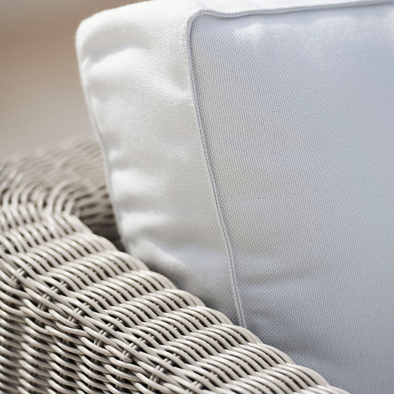 Neutral gray wicker chair with a smooth white pillow and subtle gray piping, creating a modern and chic look.