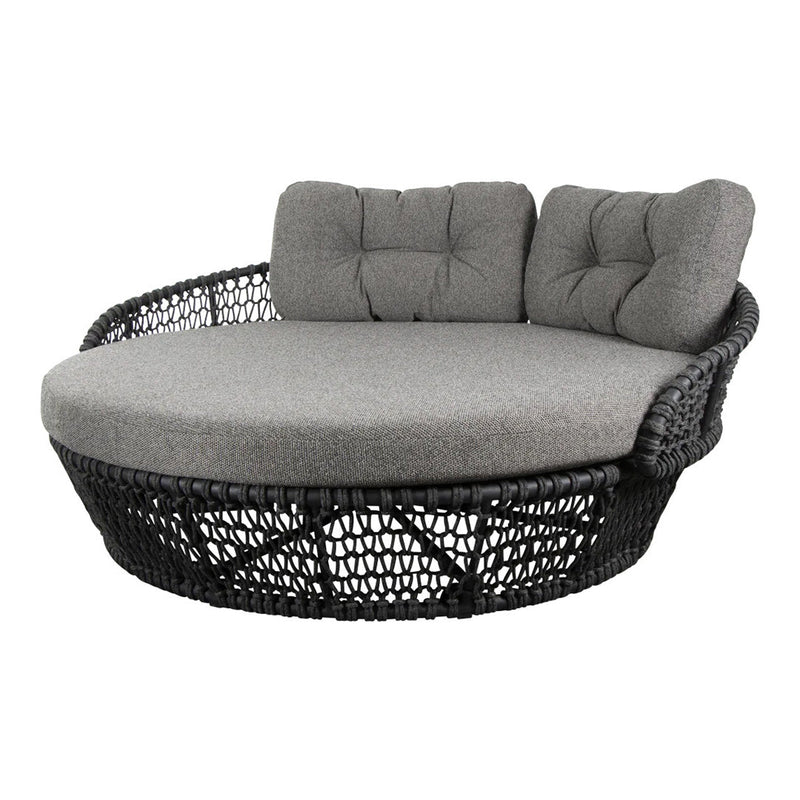 Round wicker daybed with black woven base and plush gray cushions, featuring tufted design for added comfort.