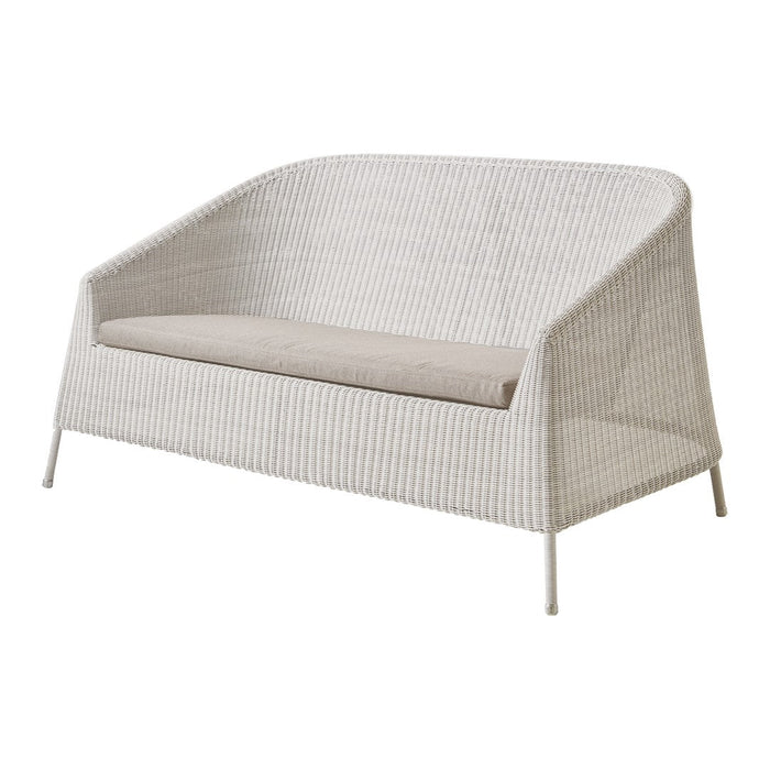 White woven loveseat with a light beige cushion, featuring a minimalist design and smooth curves. Perfect for outdoor spaces.