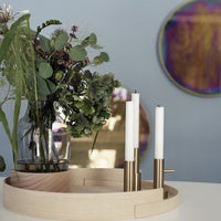 Natural wood tray with golden accents featuring white candles and vibrant greenery against a pastel blue background.