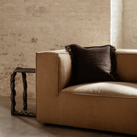 Brown sofa with a dark brown textured pillow, complemented by a sleek black side table and neutral wall backdrop.