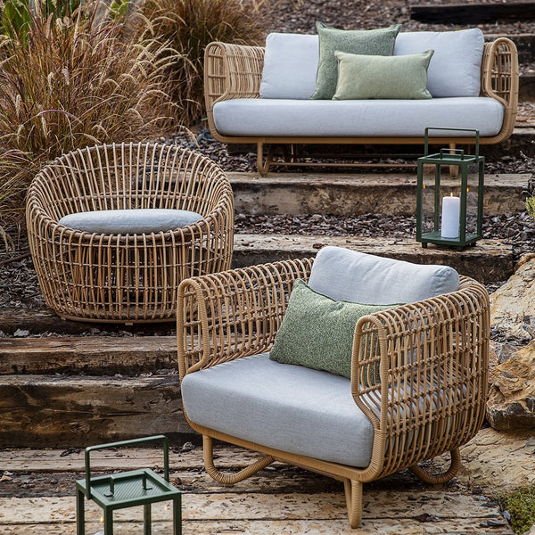 Natural wicker furniture in soft grey cushions with leafy green accents, perfect for outdoor relaxation.