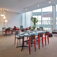 Modern dining room with red and black chairs, glass table, and neutral-toned carpet. Minimalistic design and natural light.