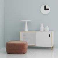 Modern white cabinet with gold accents, pink round ottoman, and minimalistic decor on a light blue wall.