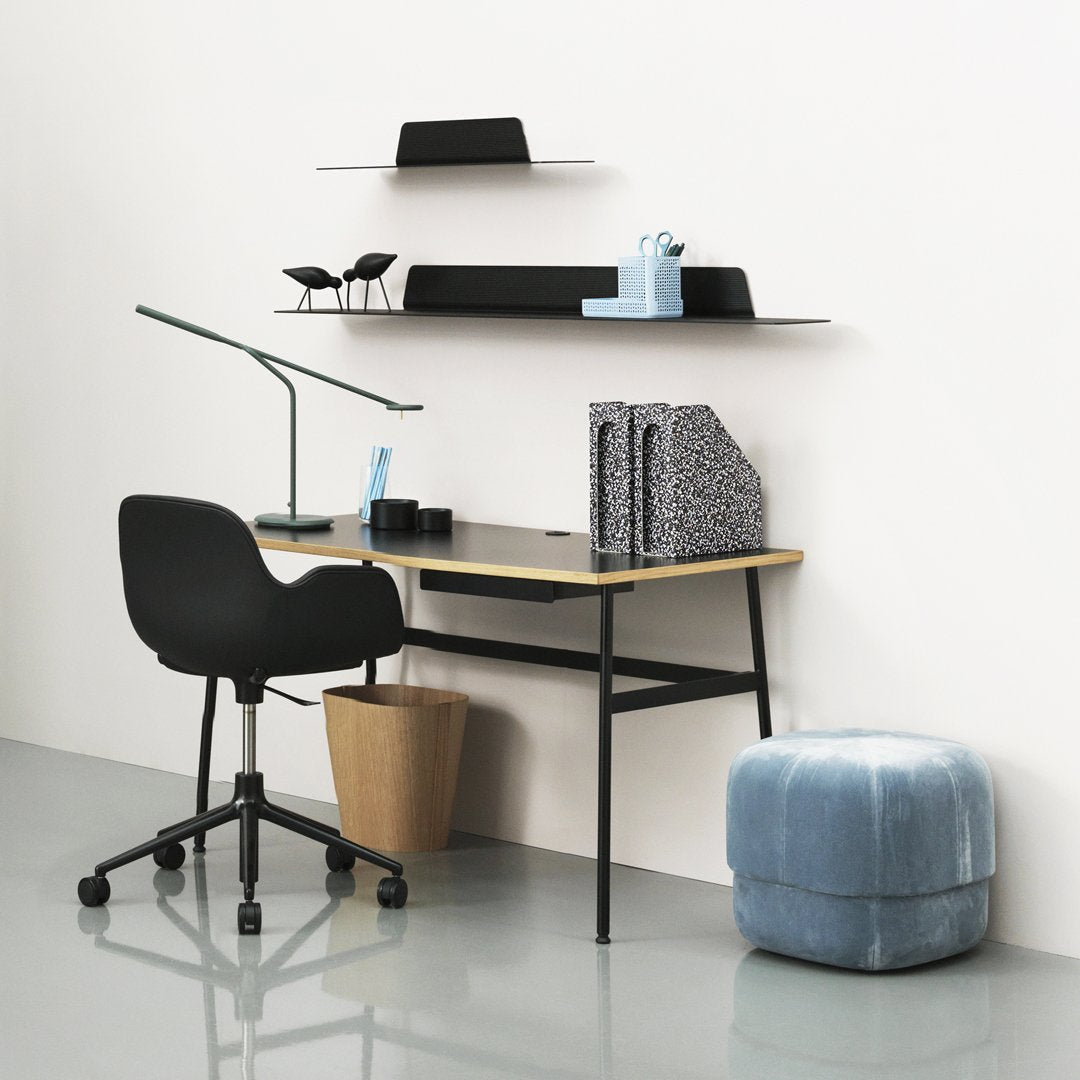 Black desk with light wood top, geometric patterns in black and white decor, soft blue pouf, modern minimalist vibe.