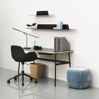 Black desk with light wood top, geometric patterns in black and white decor, soft blue pouf, modern minimalist vibe.