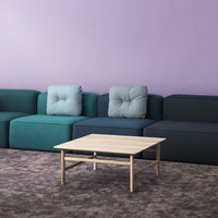 Multicolored sectional sofa in teal, navy, and gray with tufted cushions against a purple wall. Light wood coffee table in front.