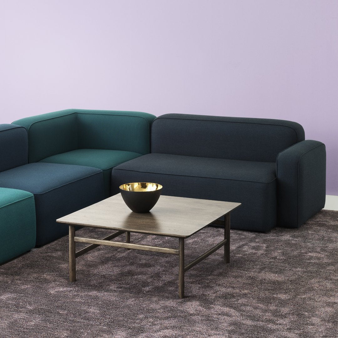 Modern sectional sofa in teal and dark blue hues, paired with a neutral-toned rug and minimalist table decor.