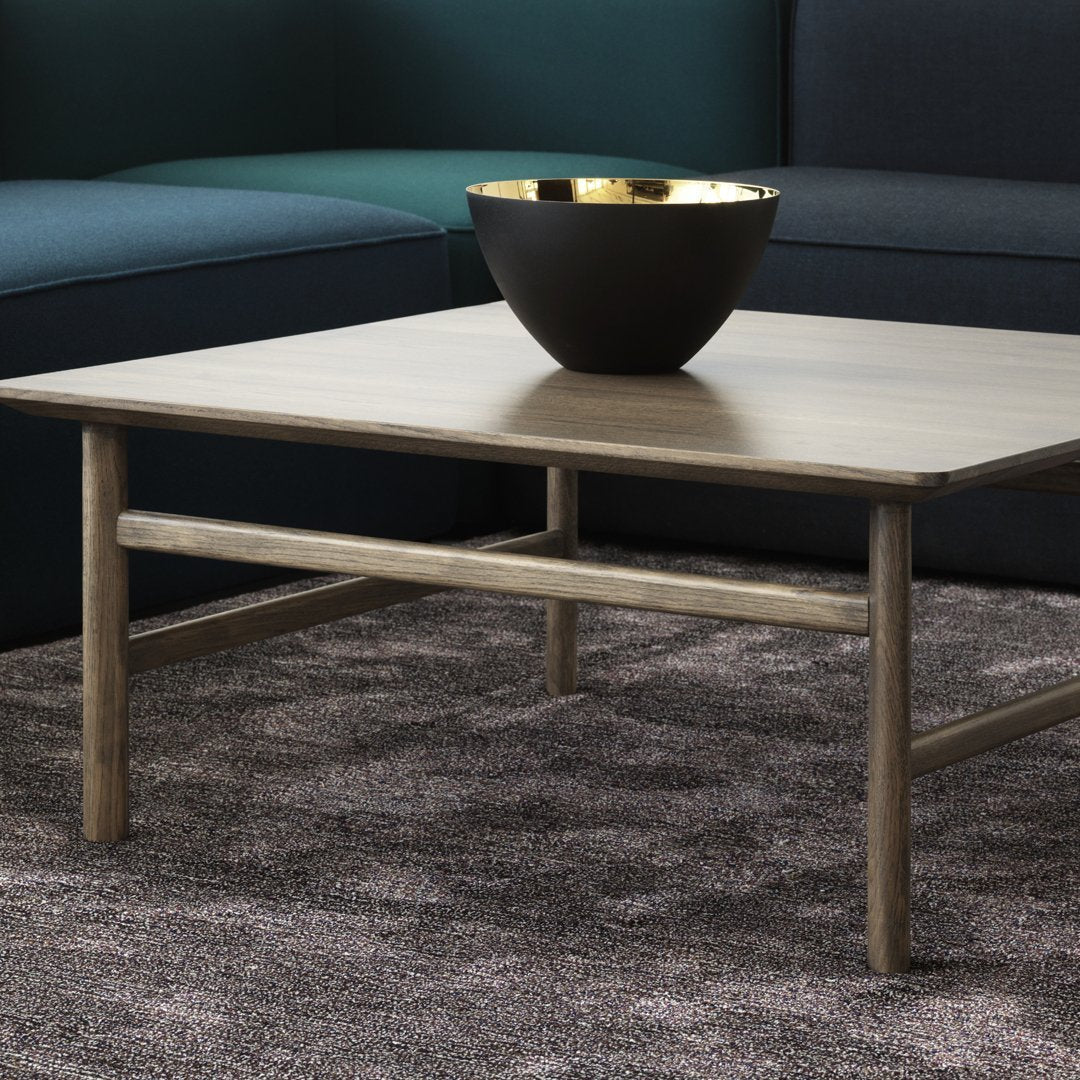 Light wood coffee table with a smooth surface and a black bowl with a gold interior, set against a textured gray carpet.