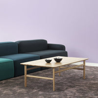 Light wood coffee table on a textured gray carpet; modern couch features deep green and navy blue sections against a soft purple wall.
