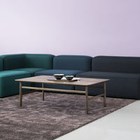 Modern sectional sofa in teal, navy, and charcoal against a pastel purple wall, featuring a neutral area rug and wooden coffee table.