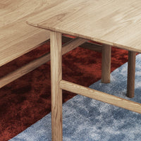 Light oak wood table with smooth edges, set against a deep red rug and blue patterned carpet.