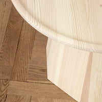 Light wood coffee table with a smooth rounded top and geometric base, showcasing natural grain patterns and soft beige tones.