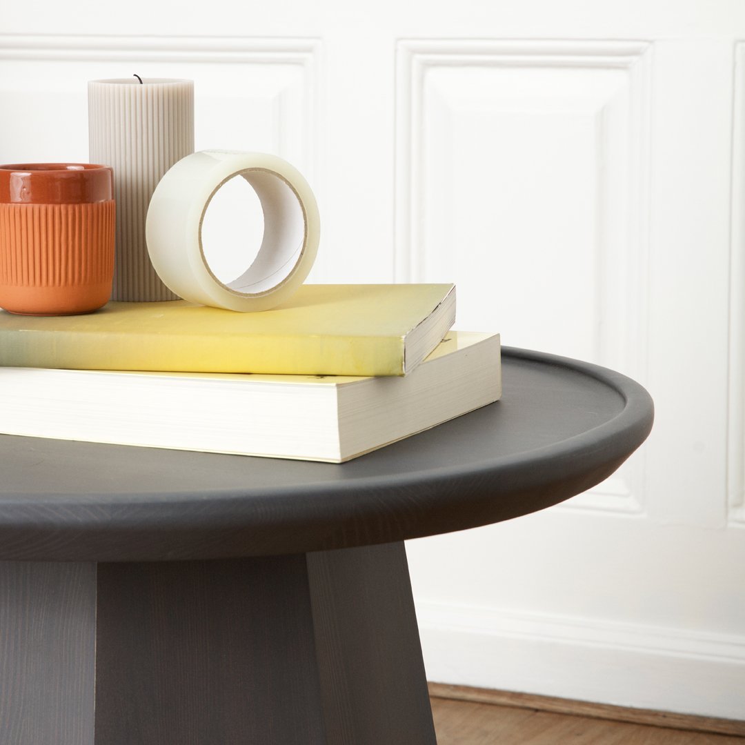 Gray round table with stacked yellow and white books, an orange candle, and a white tape roll. Elegant, modern decor.
