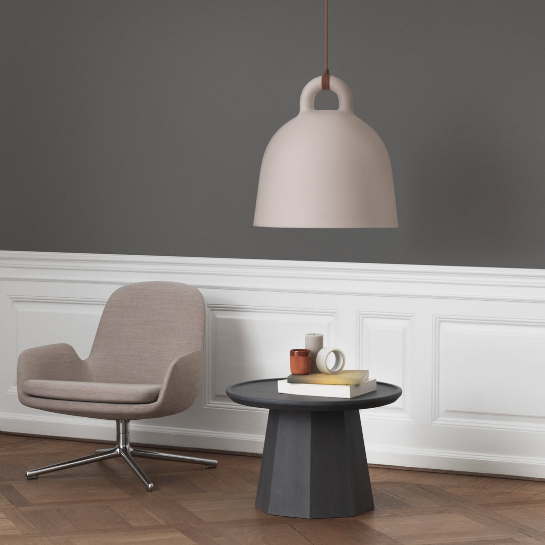 Soft pink pendant lamp above a round black table with a beige chair, set against a gray wall. Modern and minimalistic design.