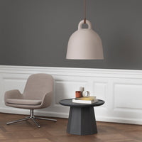 Soft pink pendant lamp above a round black table with a beige chair, set against a gray wall. Modern and minimalistic design.