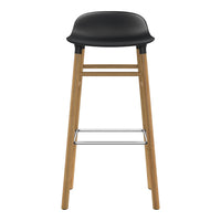Black plastic seat with natural wood legs and chrome footrest, featuring a sleek, minimalist design.