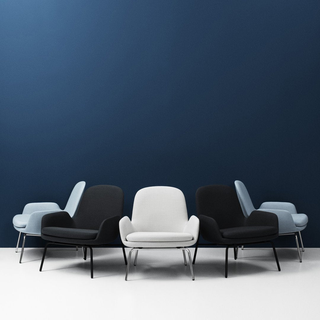 Modern chairs in black, white, and muted blue against a deep blue wall, showcasing sleek lines and contemporary design.