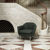 Green curved armchair on marble floor with geometric patterns and elegant staircase backdrop.