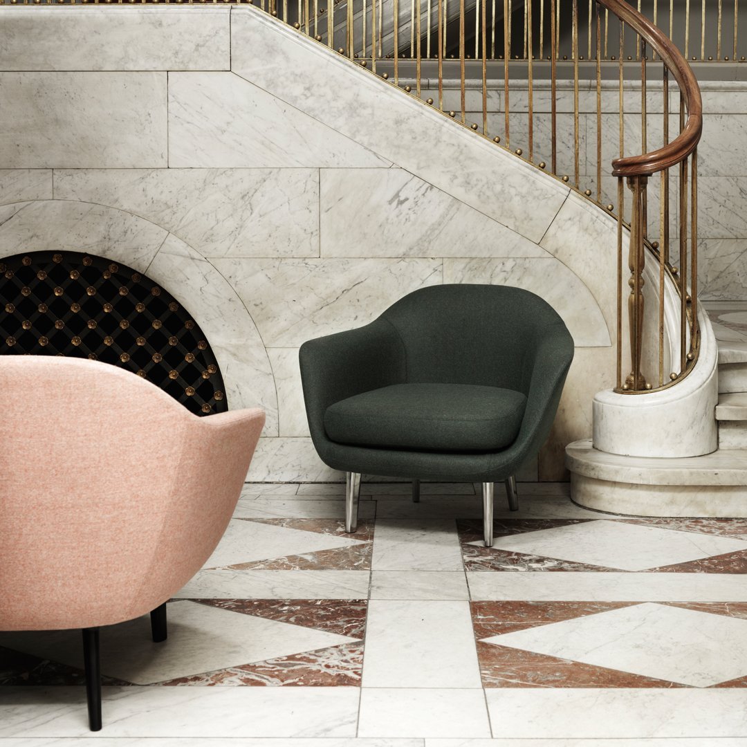 "Green and pink upholstered chairs with smooth curves against a marble floor and elegant staircase backdrop."