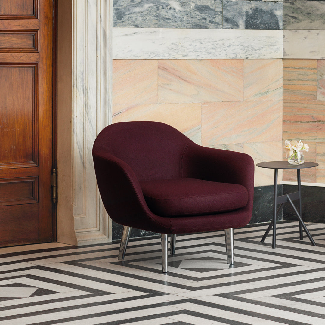 Burgundy velvet armchair on black and white geometric patterned floor with marble wall background.