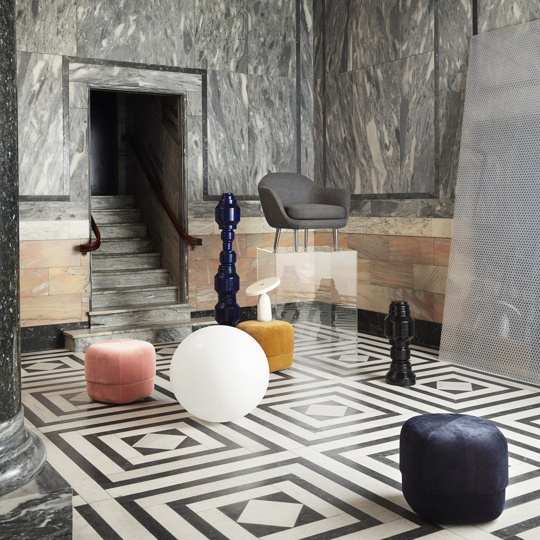 Colorful poufs in pink, white, yellow, and blue on a black and white geometric patterned floor in an elegant setting.