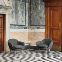 Two gray armchairs on a bold black-and-white patterned floor against a marble and wooden backdrop.