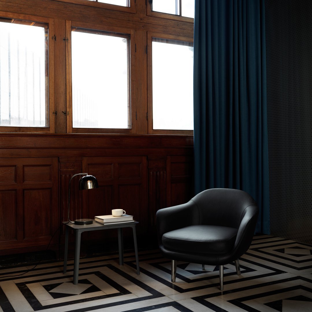 Black chair on geometric black and white patterned floor, with deep blue curtains and warm wooden accents.