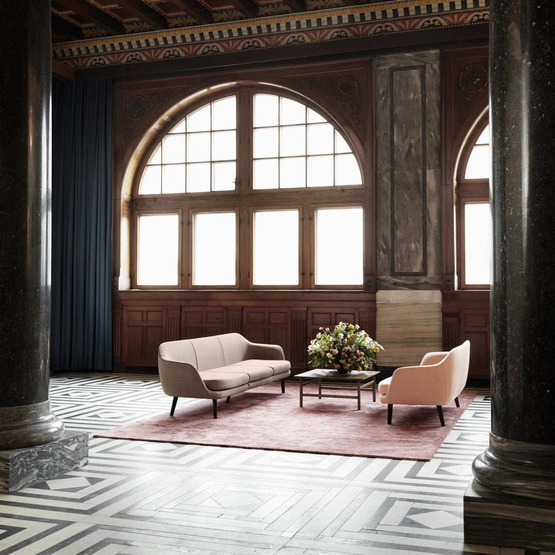 Soft beige couch and blush armchair on a pink rug, with bold black and white geometric flooring, set in an elegant space.