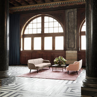 Soft beige couch and blush armchair on a pink rug, with bold black and white geometric flooring, set in an elegant space.