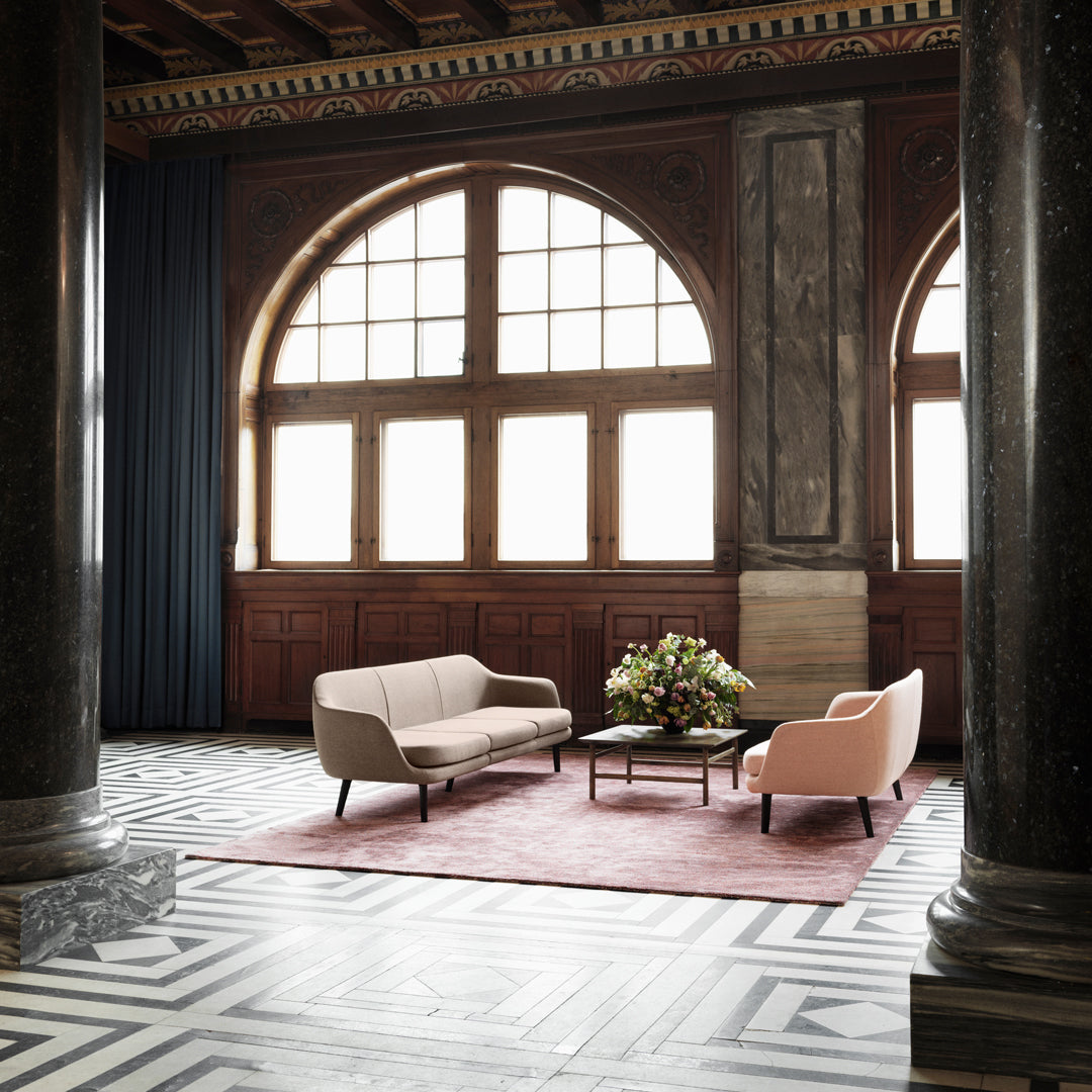 Stylish pink and beige sofas on a geometric patterned floor with a pink rug, set against elegant dark wood features.