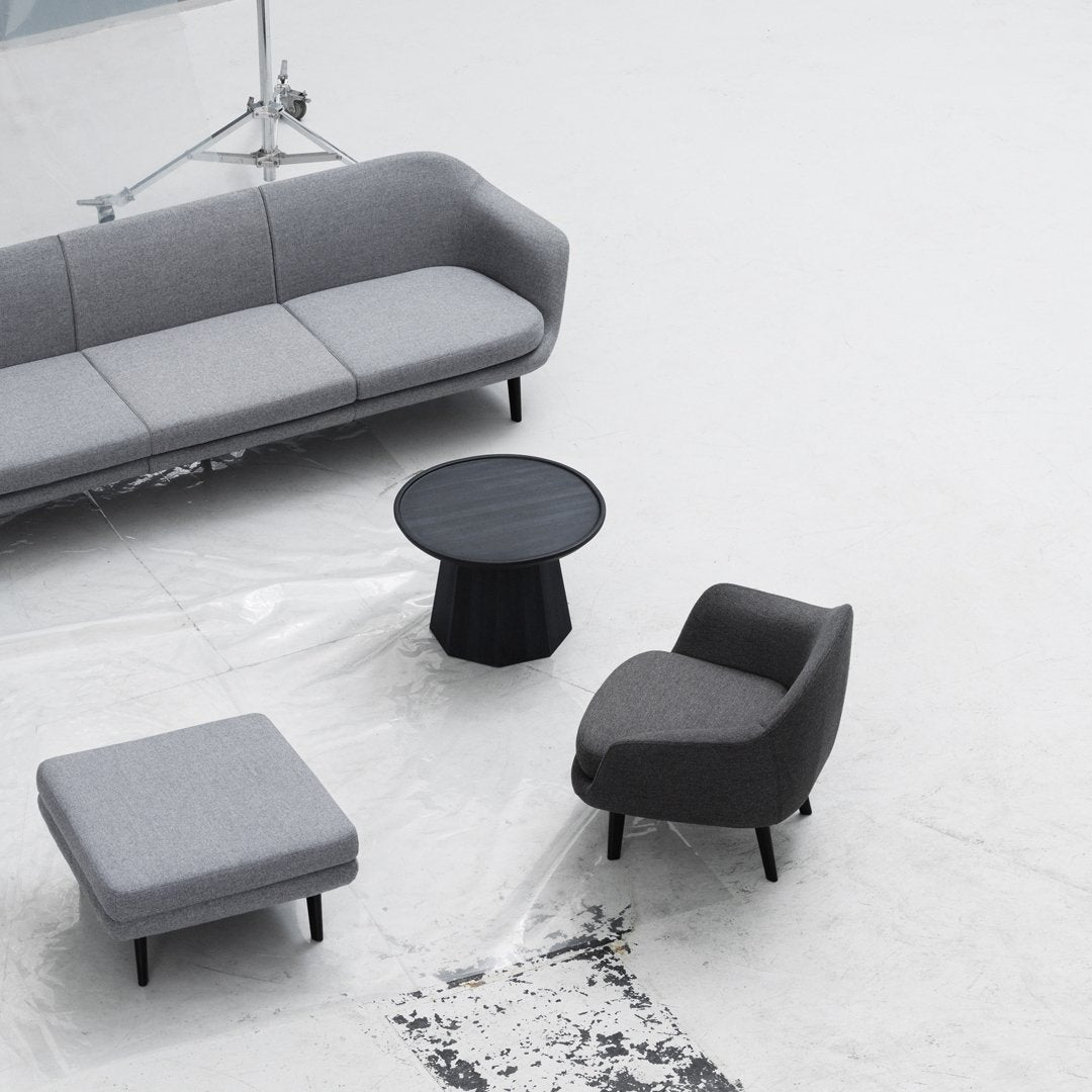 Modern gray sofa set with textured fabrics and black, round coffee table on a minimalist white floor.