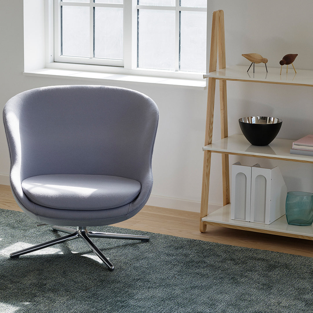 Lavender upholstered chair with smooth contours, set against a neutral-toned wooden floor and light gray rug.