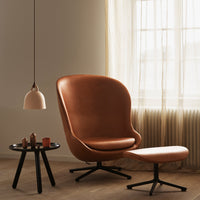"Rust-orange leather chair with matching ottoman, black table, and modern pendant light against soft beige backdrop."