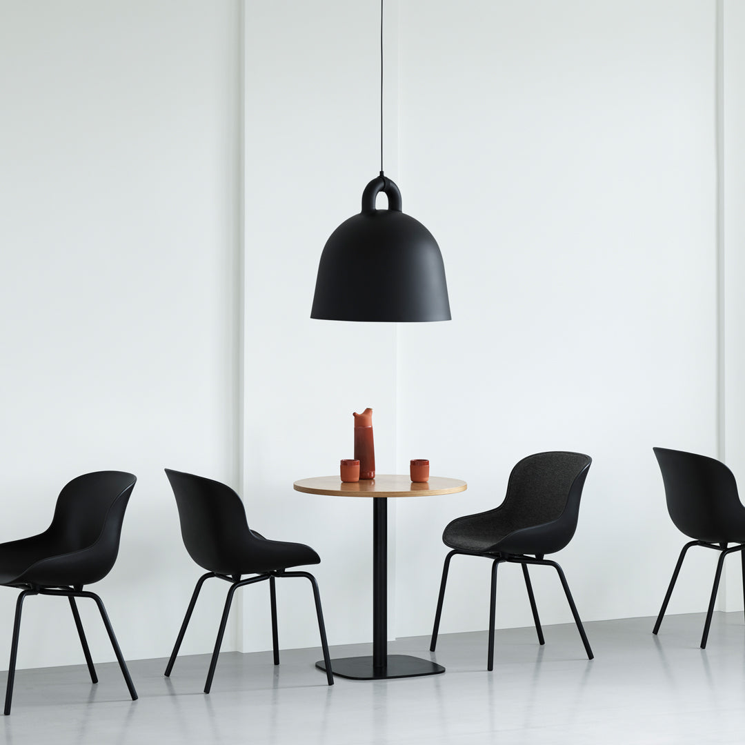 Black pendant lamp with smooth finish, surrounded by sleek black chairs and a minimalist round wooden table.
