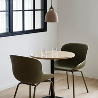 "Round wooden table with two olive green chairs and a pink pendant light against a minimalist white background."