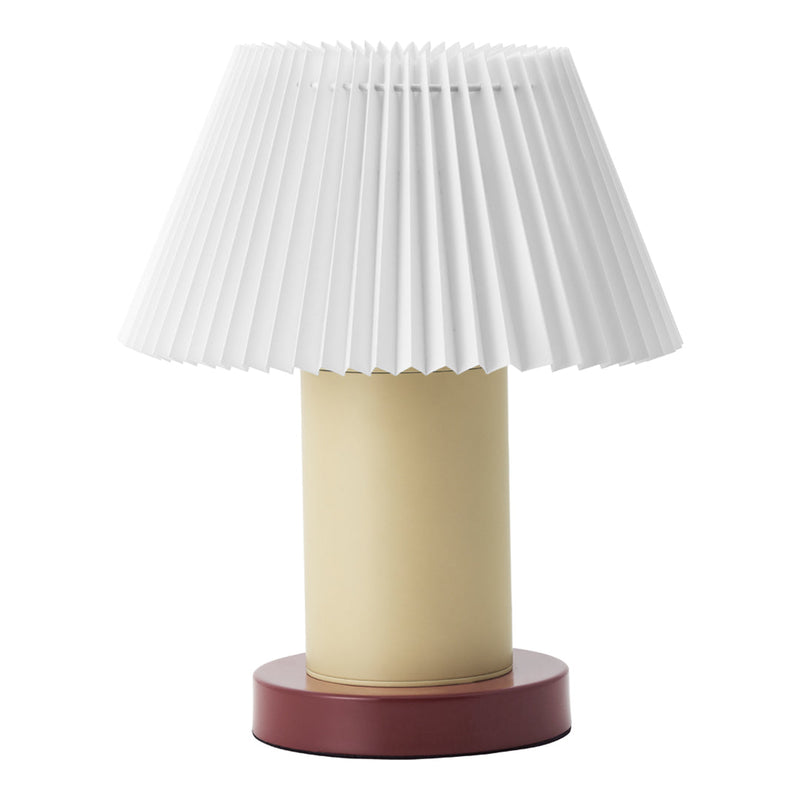 White pleated lampshade atop a cream base with a burgundy round pedestal. Modern and stylish lighting design.
