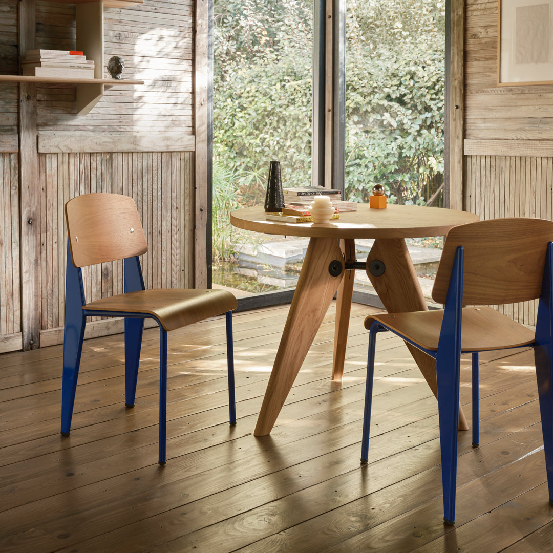 Wooden table with natural finish, paired with chairs featuring light wood seats and vibrant blue legs. Modern design.