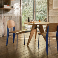 Wooden table with natural finish, paired with chairs featuring light wood seats and vibrant blue legs. Modern design.