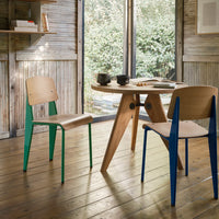 "Wooden dining table with green and blue upholstered chairs, featuring natural wood texture and a minimalist design."