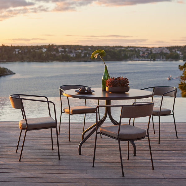 Modern round table with black metal frame and beige chairs, set against a serene lakeside backdrop at sunset.