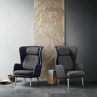 Two modern armchairs in navy and gray upholstery, featuring a geometric backdrop with intricate wood patterns.