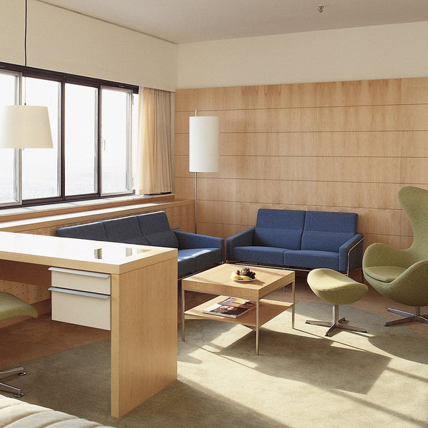 Modern living room featuring blue sofas, green accent chairs, light wood accents, and neutral beige tones.