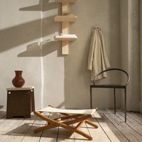 "Neutral-toned room with wooden textures, a cream fabric stool, black chair, and earthy brown vase."