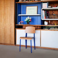 Natural wood chair with a blue metal frame, set against a vibrant blue and wooden backdrop. Stylish and modern design.