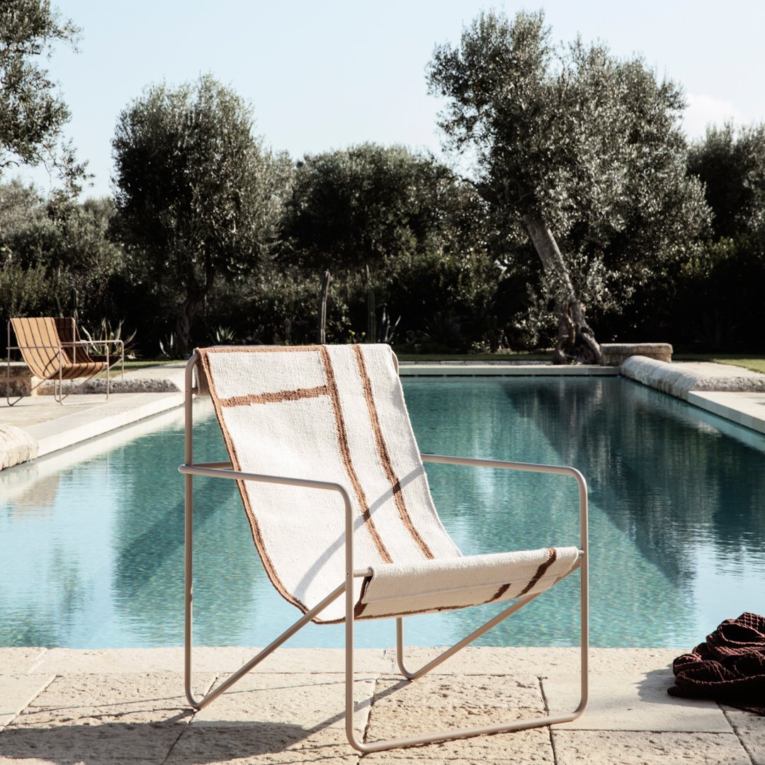Beige lounge chair with brown stripes, set by a serene pool surrounded by greenery.