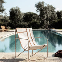 Beige lounge chair with brown stripes, set by a serene pool surrounded by greenery.