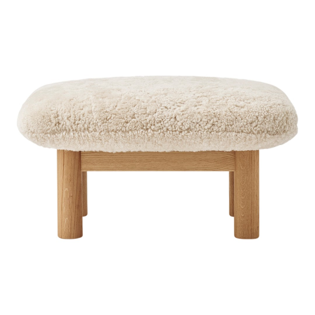 Cream faux sheepskin ottoman with natural wood legs, featuring a soft, textured surface and rounded shape.